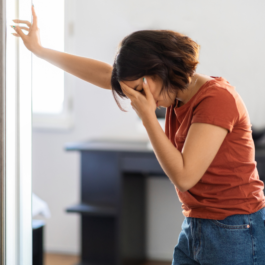 A woman leaning against a glass door, feeling dizzy.